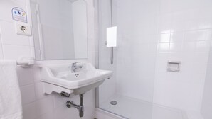 Une salle de bain avec un lavabo blanc, un miroir, une cabine de douche en verre et une serviette blanche accrochée au mur.