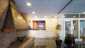 A lobby with a brick wall, a black marble floor, a wooden bench, a television screen, and a potted plant. - Azuline Hotel S'anfora & Fleming (Sant Antoni de Portmany)