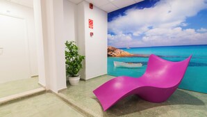 A reception area with a beach mural, a potted plant, and a pink chair. - Azuline Hotel S'anfora & Fleming (Sant Antoni de Portmany)