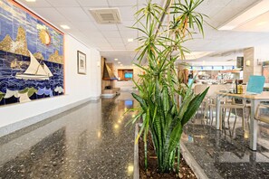 A lobby with a tiled mural, a reception desk, a digital screen, and a seating area with tables and chairs. - Azuline Hotel S'anfora & Fleming (Sant Antoni de Portmany)