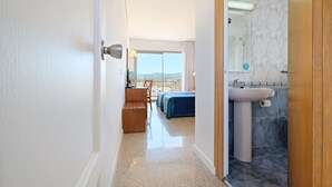 Une chambre d’hôtel avec un lit, un banc en bois, une salle de bain avec un lavabo et un miroir, et une vue sur l’extérieur.