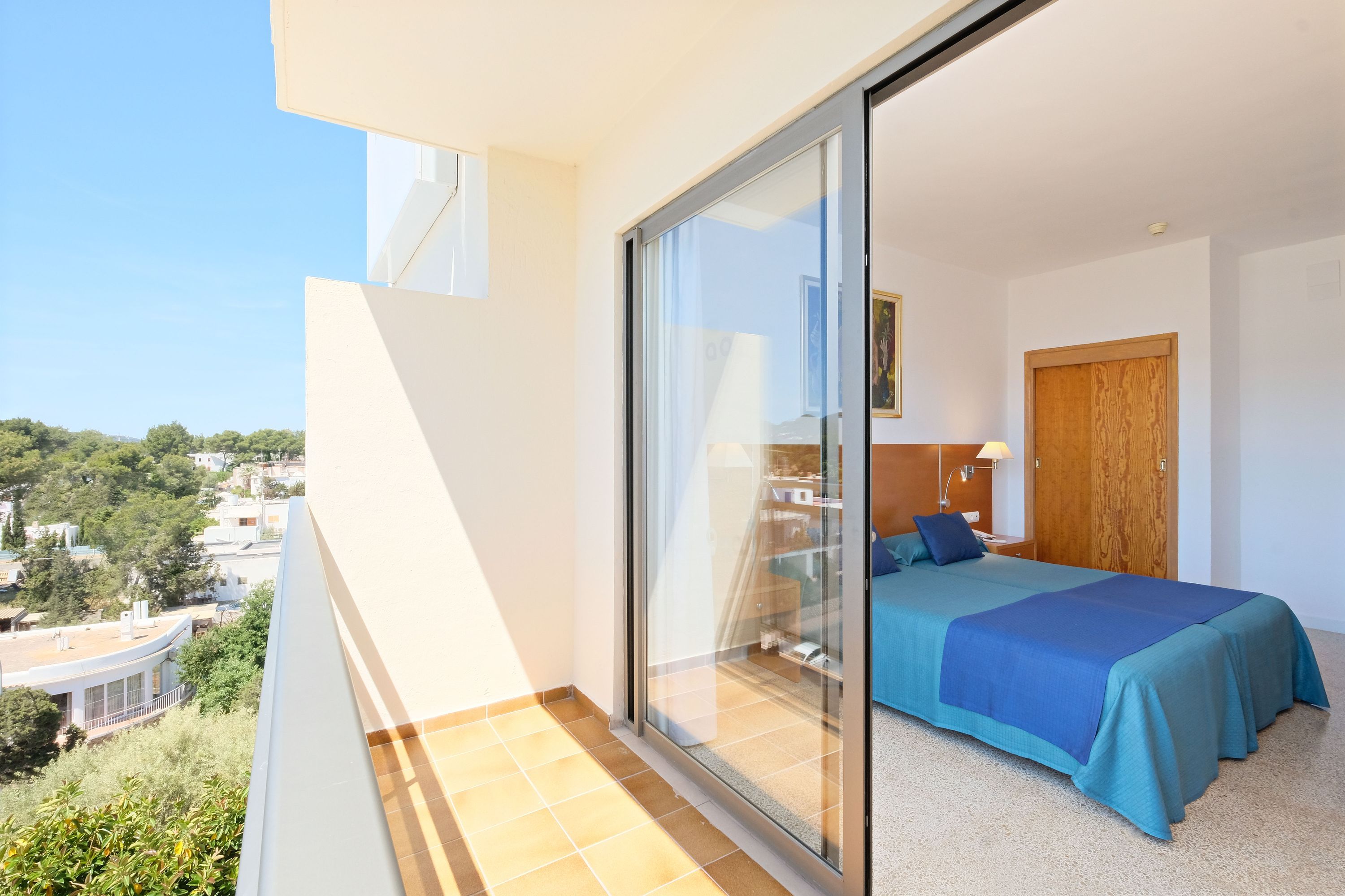 Un balcón con puerta de vidrio que da a un dormitorio con cama y mesita de noche.