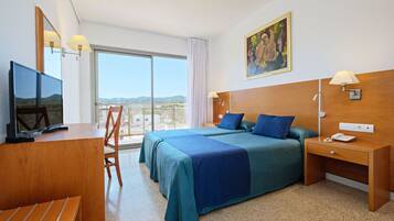 Una camera d'albergo con un letto grande, una scrivania con televisore, una sedia, un comodino con lampada e un quadro appeso al muro.