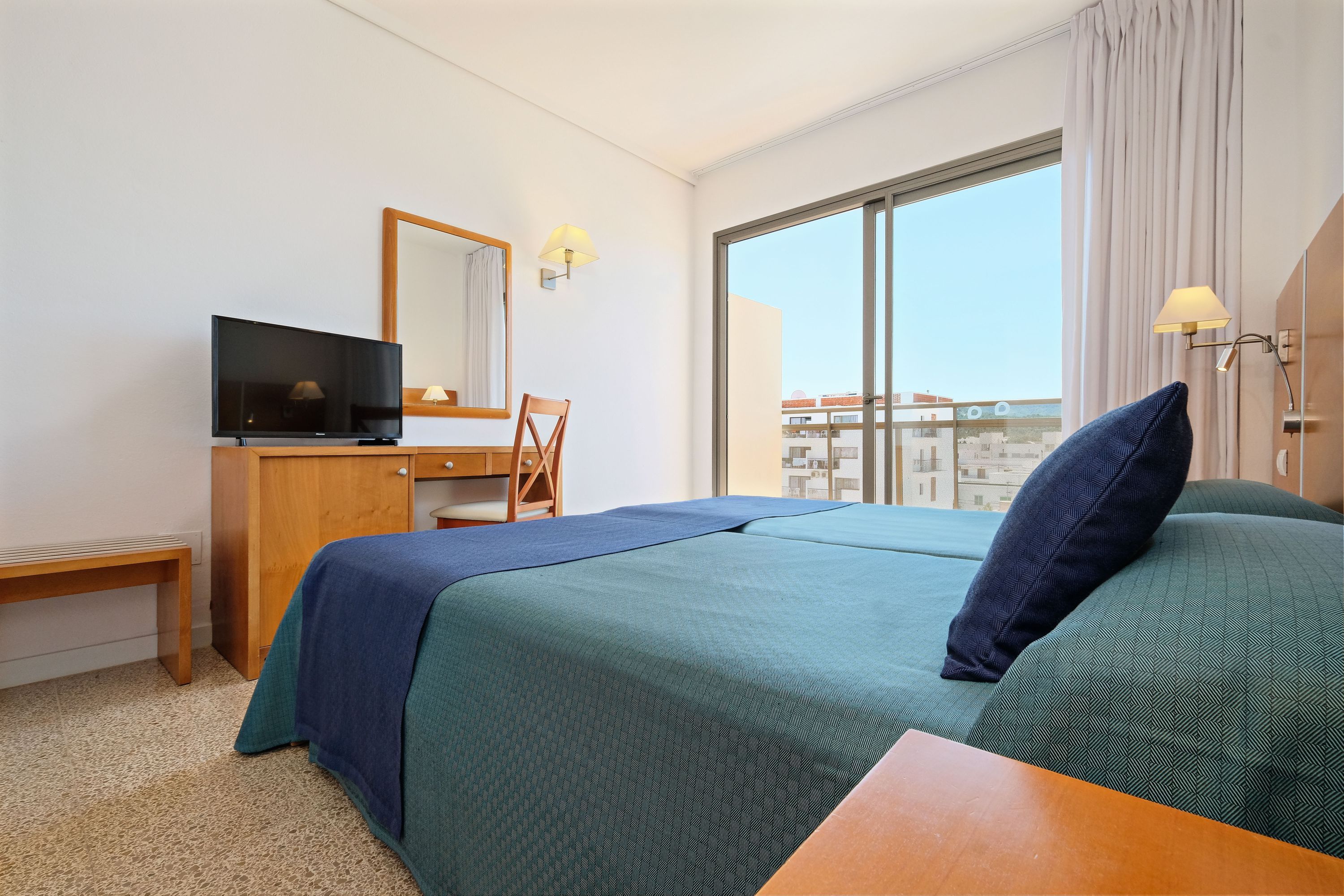 Een hotelkamer met een bed, een bureau, een televisie en een groot raam met uitzicht op de stad.