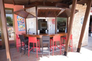 A bar with a stone wall, red chairs, and a wooden counter. - Azuline Hotel S'anfora & Fleming (Sant Antoni de Portmany)