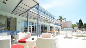 An outdoor seating area with wicker furniture and a glass-enclosed building in the background. - azuLine Hotel Pacific (Sant Antoni de Portmany)