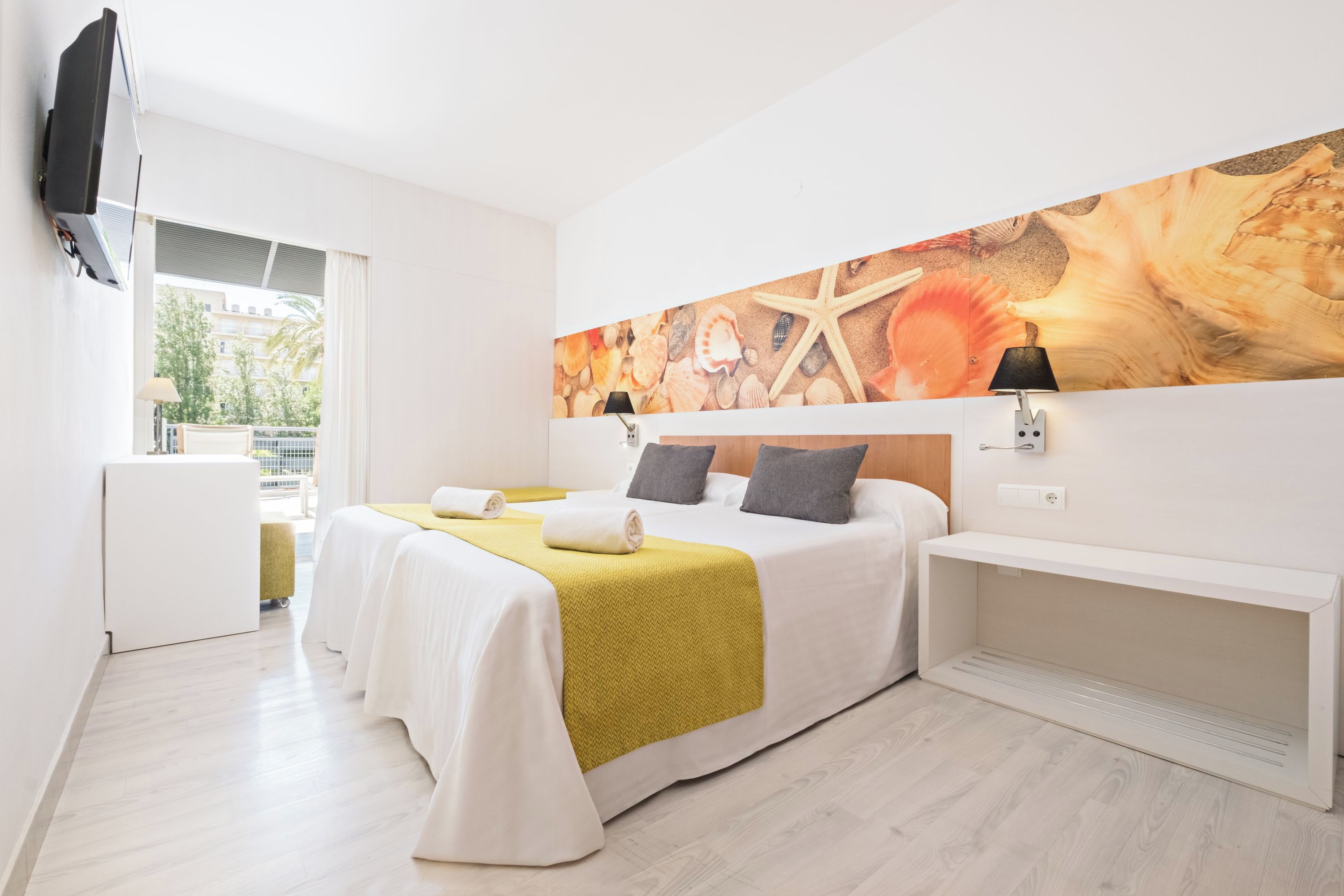 A hotel room with a bed, a desk, a TV, and a large wall mural.