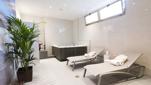 A modern spa room with two reclining chairs, a massage table, a hot tub, and a potted plant. - azuLine Hotel Pacific (Sant Antoni de Portmany)
