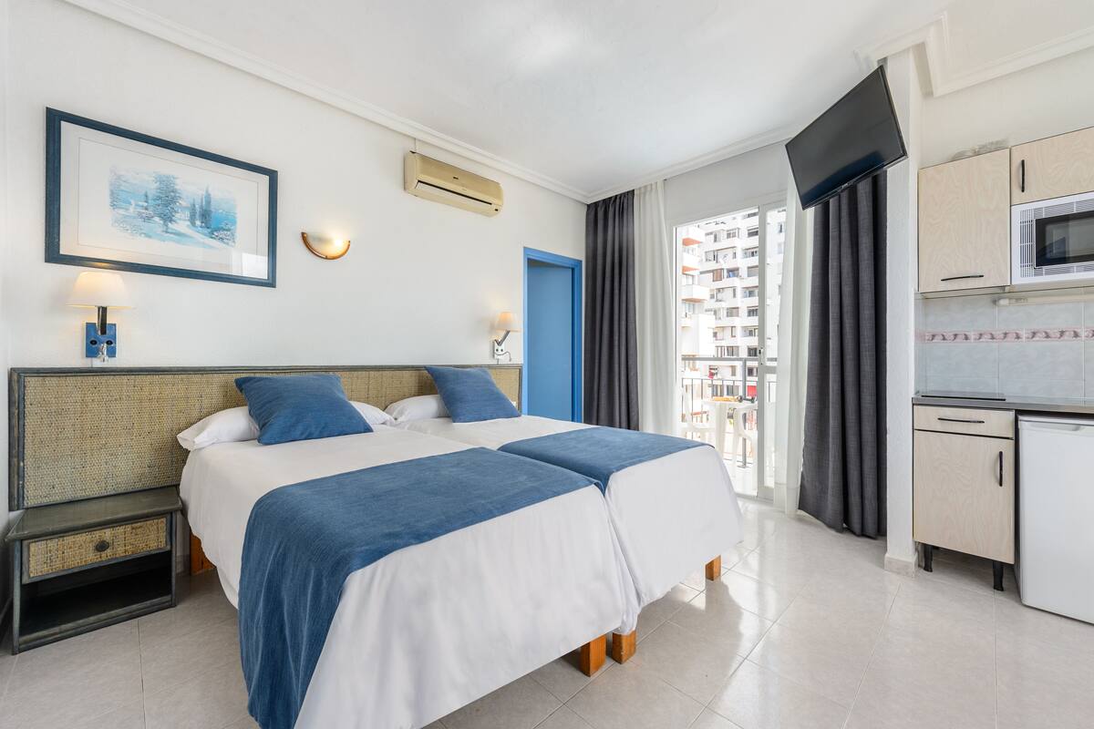 Une chambre d’hôtel avec deux lits, une kitchenette, une télévision et un balcon offrant une vue sur la ville.