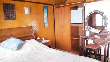 A bedroom with a bed, a wooden wardrobe, a vanity with a mirror, and a wall-mounted light fixture.