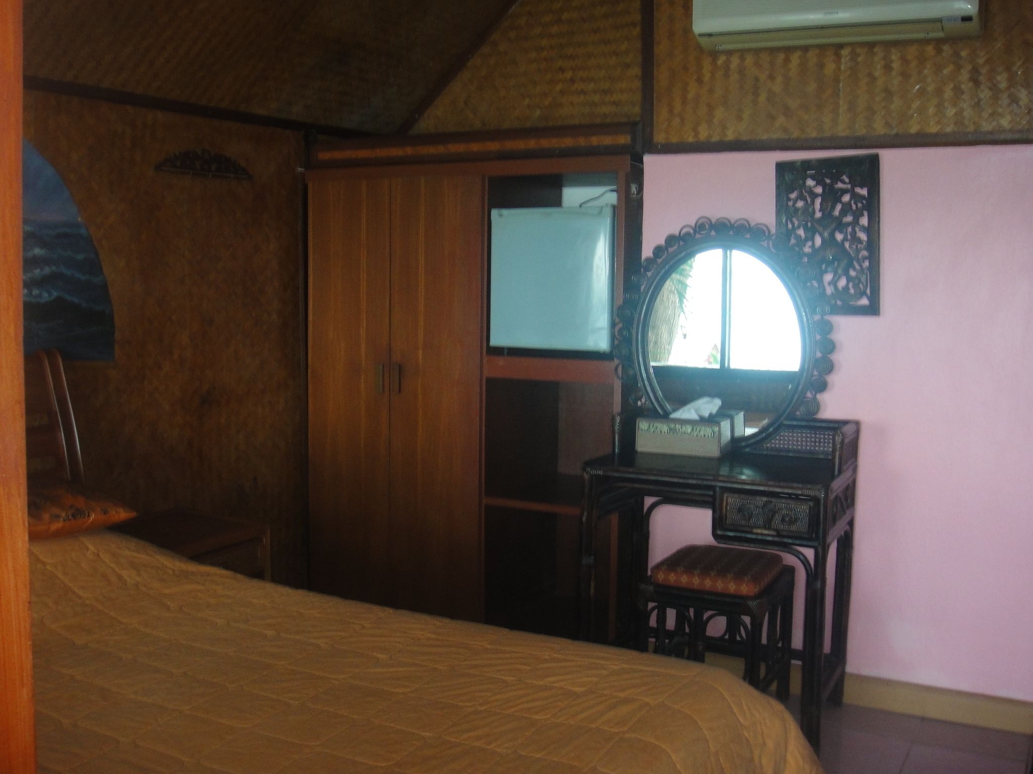 A bedroom with a bed, a wooden wardrobe, a vanity with a mirror, and a small stool.