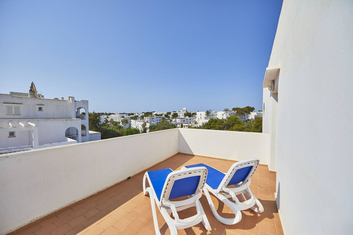 Un balcón con dos sillones blancos y vista a una zona residencial.