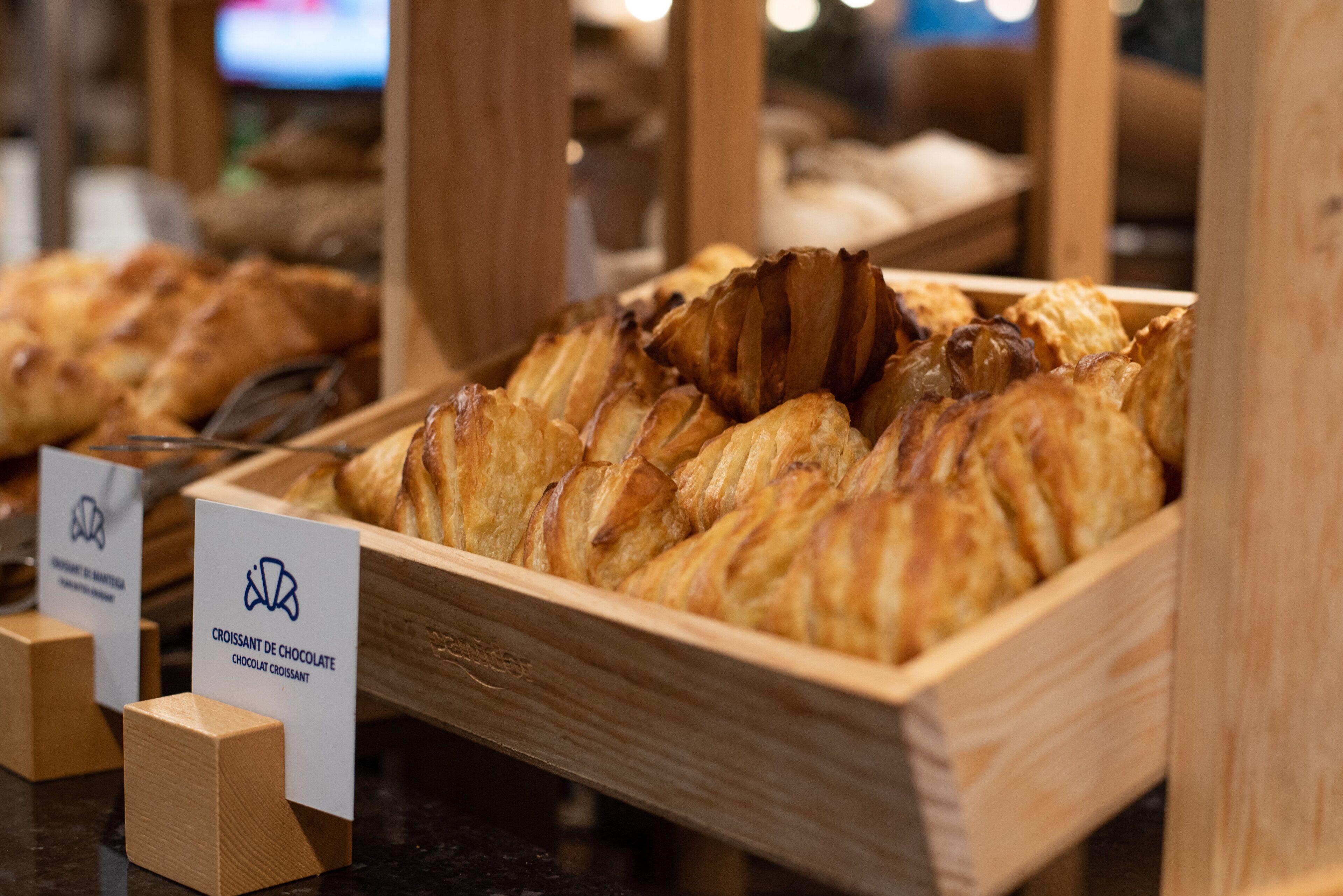 Une présentation de croissants dans une boîte en bois, avec une pancarte indiquant qu’il s’agit de croissants au chocolat.