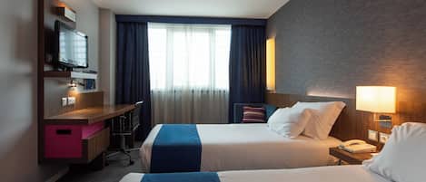 A hotel room with two beds, a desk, a television, and a window with curtains.
