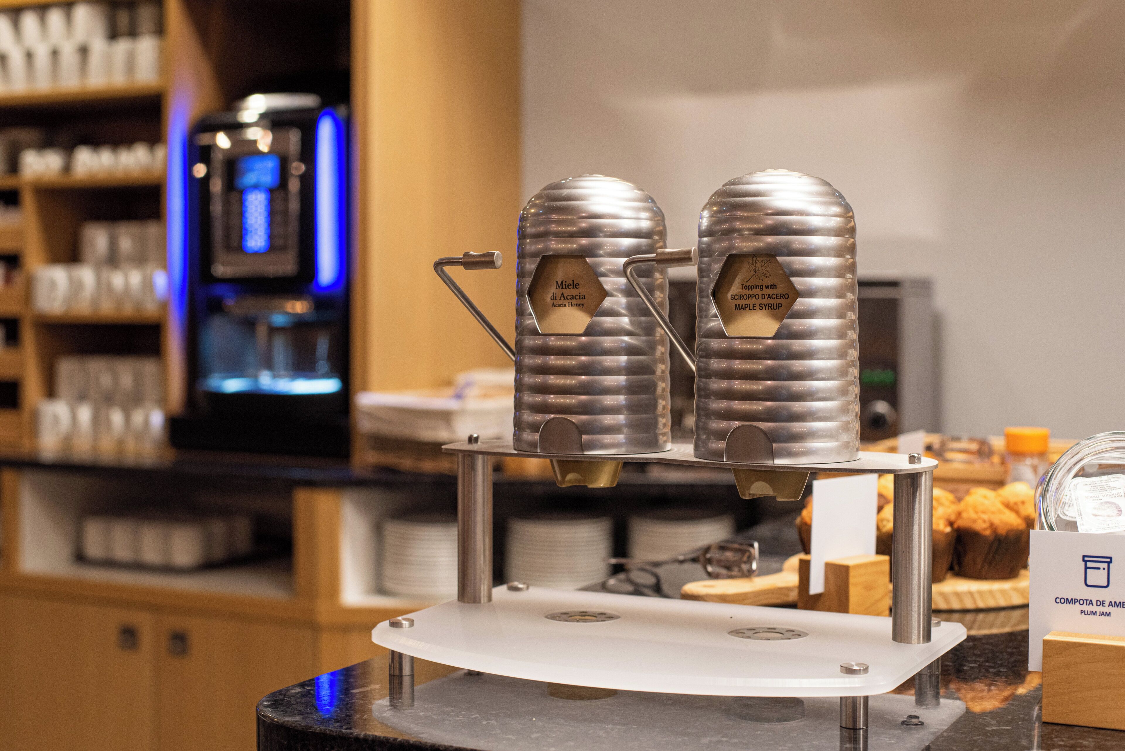 Een koffieapparaat met twee zetgroepen op een aanrecht, een koffieapparaat op de achtergrond en een presentatie van gebak.