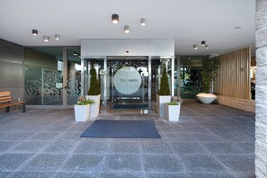 A modern entrance with a glass door, a bench, and potted plants.