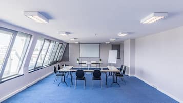 Un salón de conferencias con una mesa larga, sillas, una pantalla de proyector y grandes ventanales.