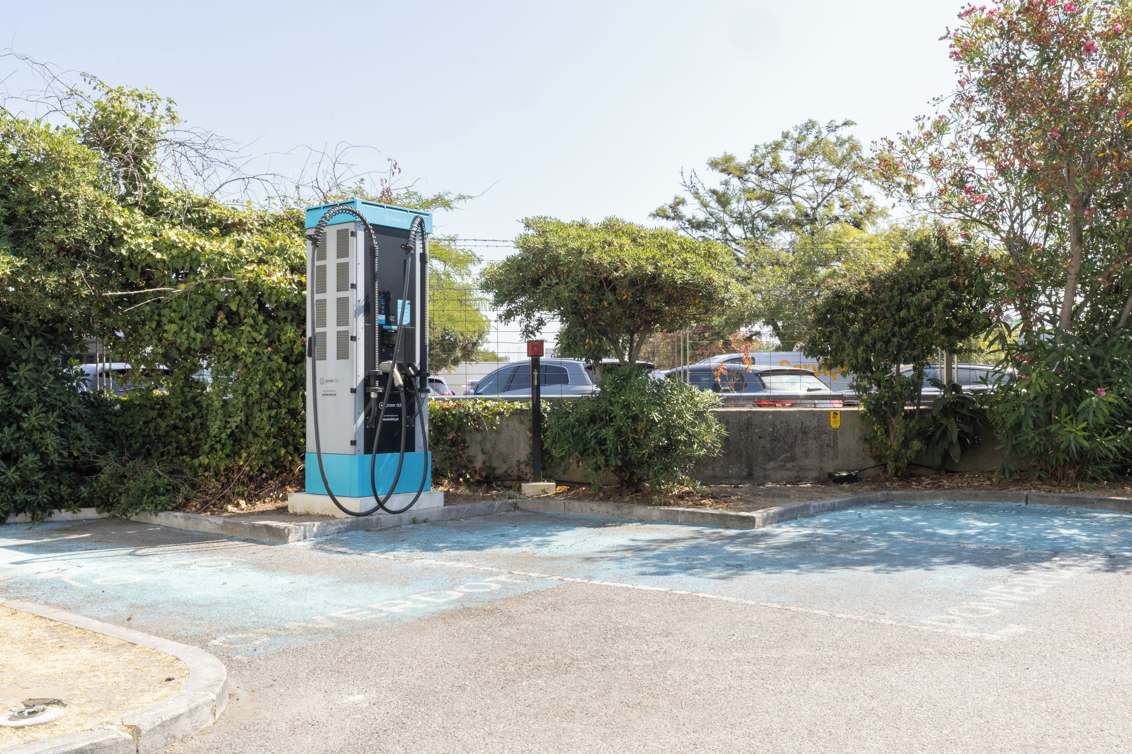 Un estacionamiento con una estación de carga, un muro de concreto y árboles.