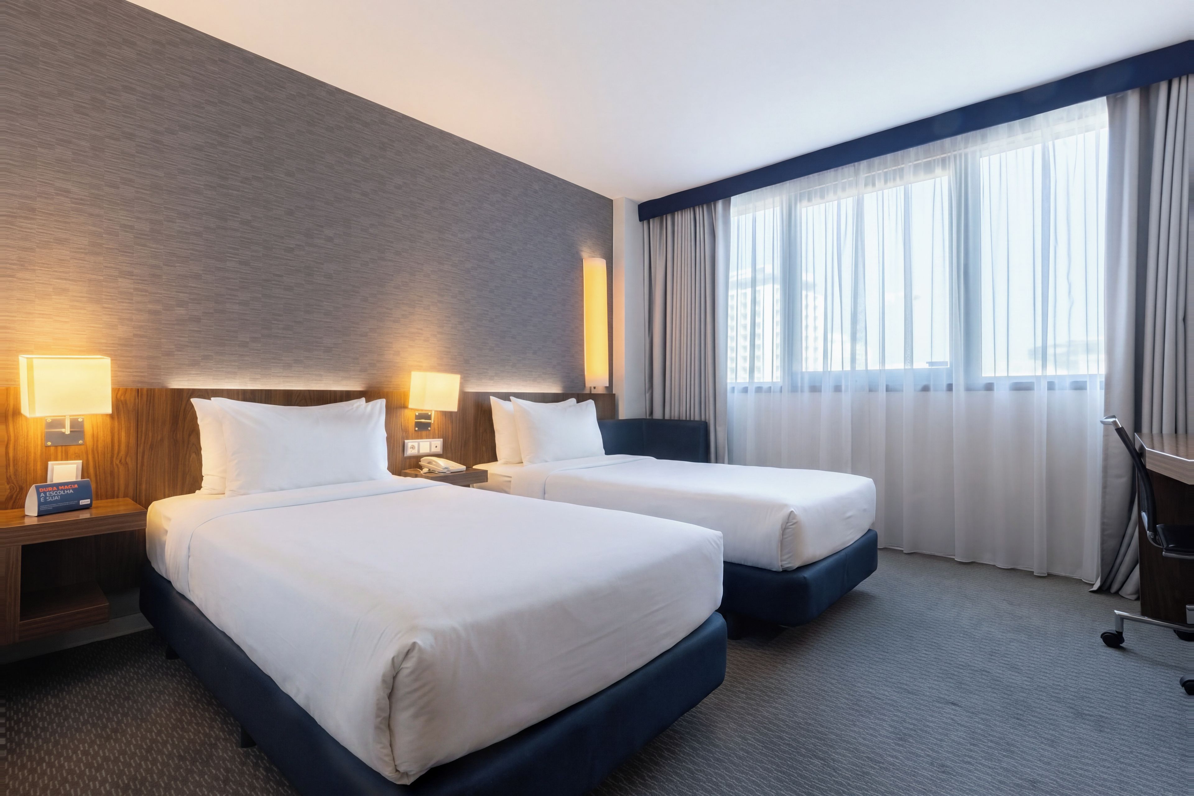 Hotellihuone, jossa on kaksi sänkyä, työpöytä ja tuoli.
