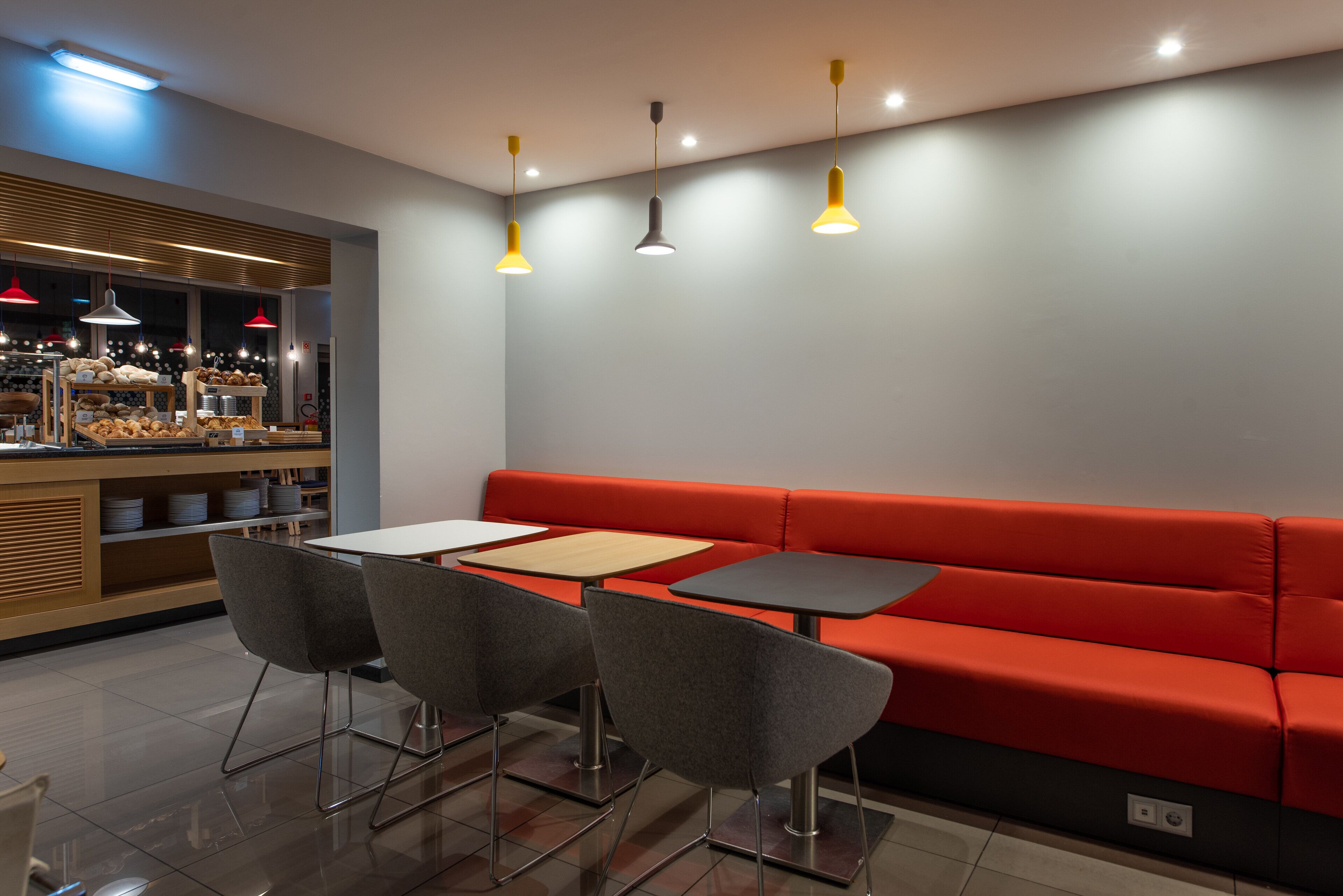Un café moderne avec un coin salon doté de banquettes rouges, ainsi que des tables et des chaises.