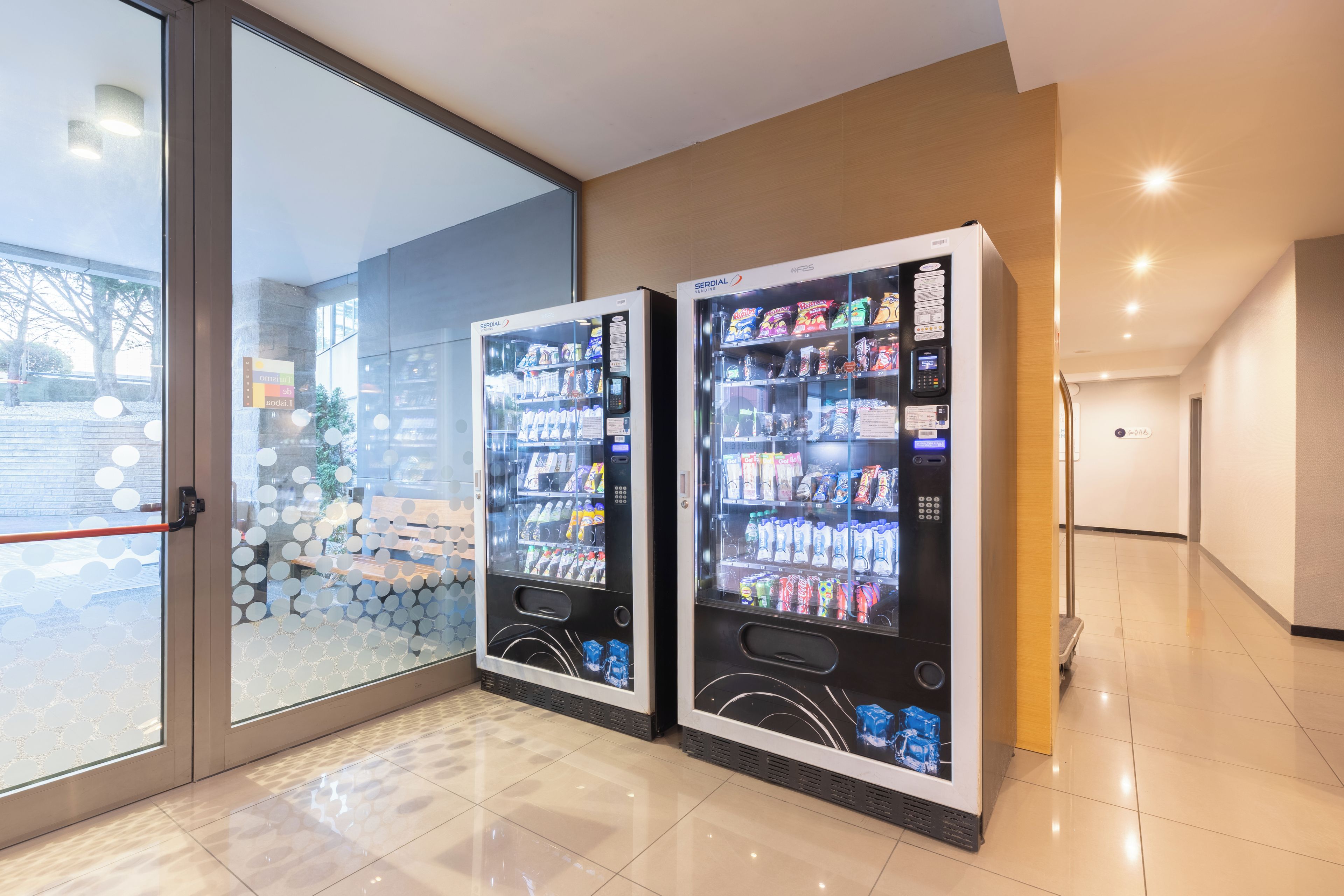 Deux distributeurs automatiques dans un espace intérieur moderne, avec une porte vitrée donnant sur l’extérieur.