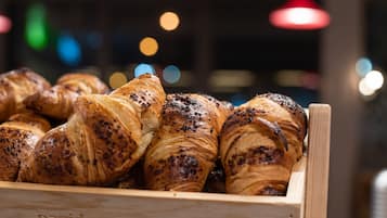 Een houten doos gevuld met diverse gebakjes, waaronder croissants en broodjes.