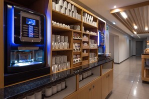 A self-service coffee station with a digital ordering system, shelves of mugs and plates, and a clean, modern interior.