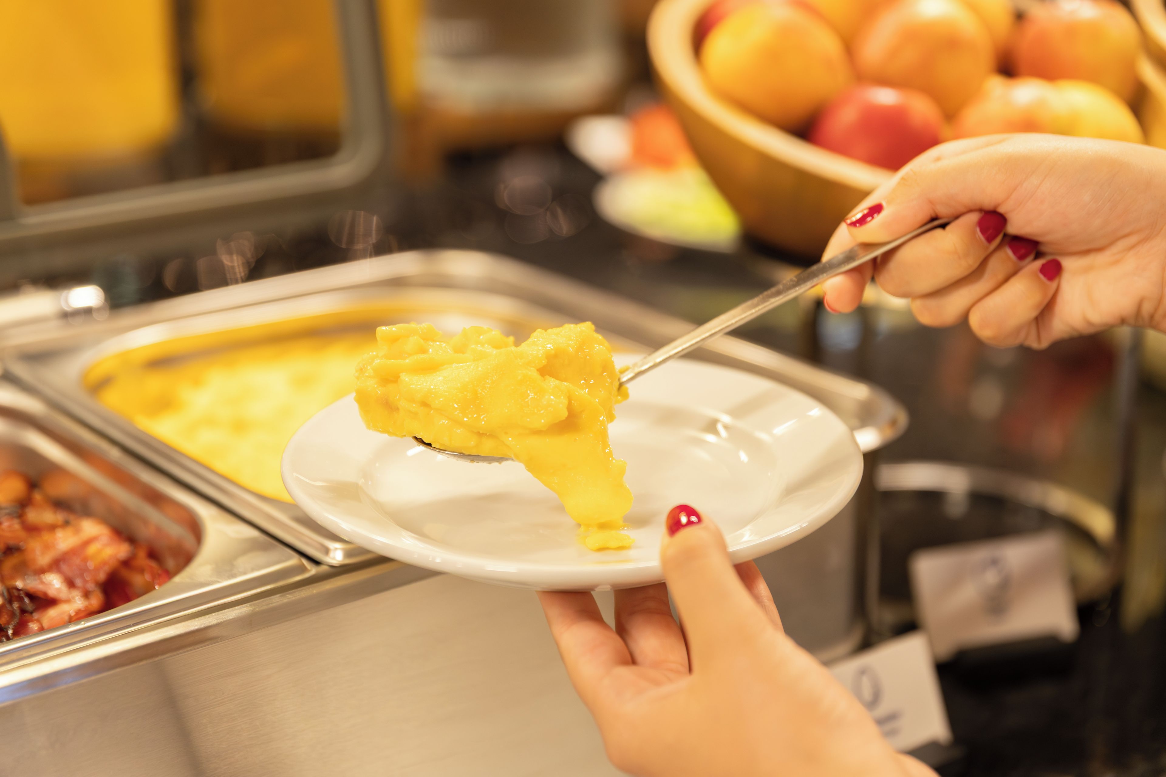 A buffet with various food options, including a dish with yellow sauce and a bowl of fruit.