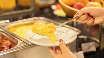 A buffet with various food options, including a dish with yellow sauce and a bowl of fruit.