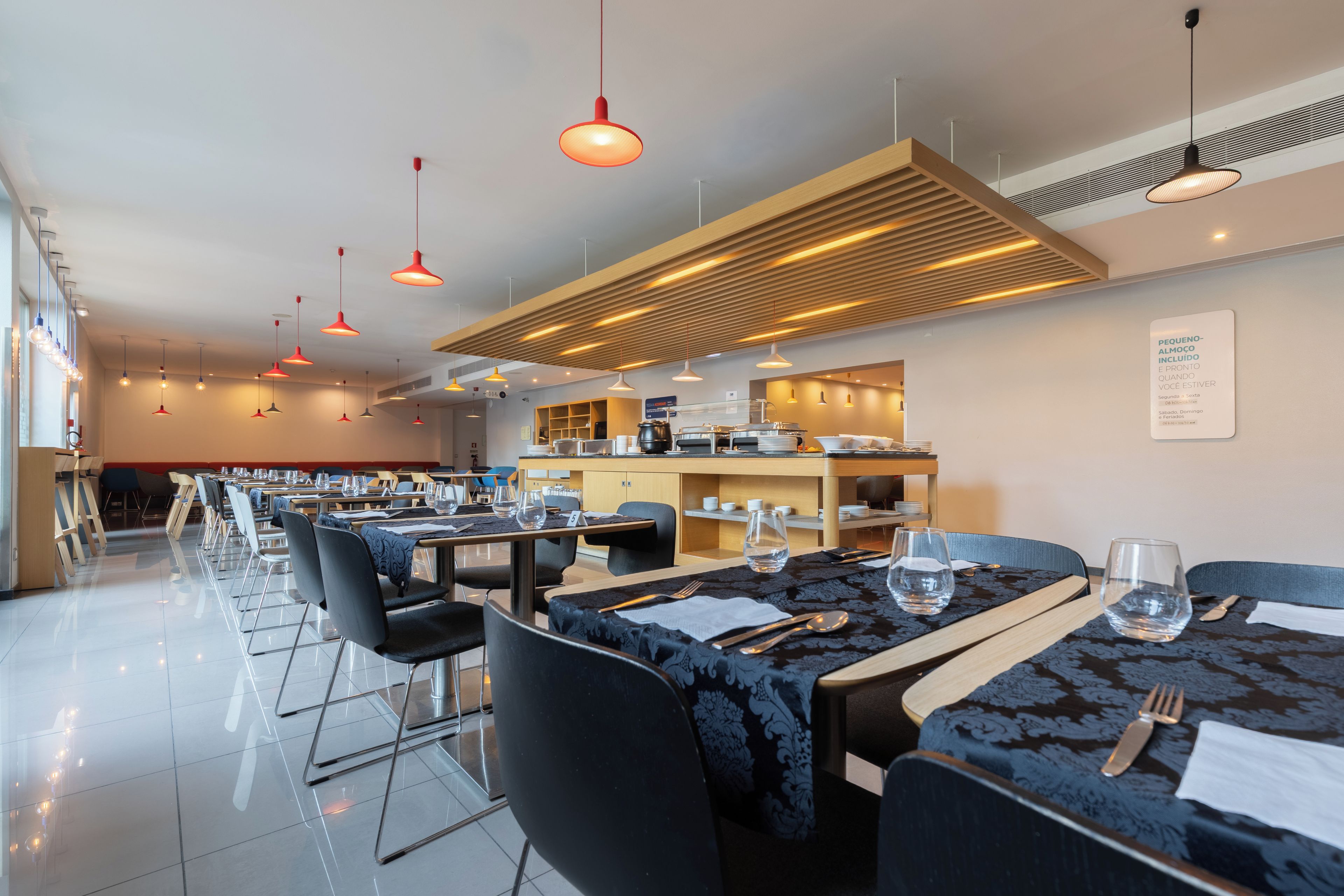 A modern dining area with multiple tables and chairs, overhead lighting, and a kitchen area in the background.