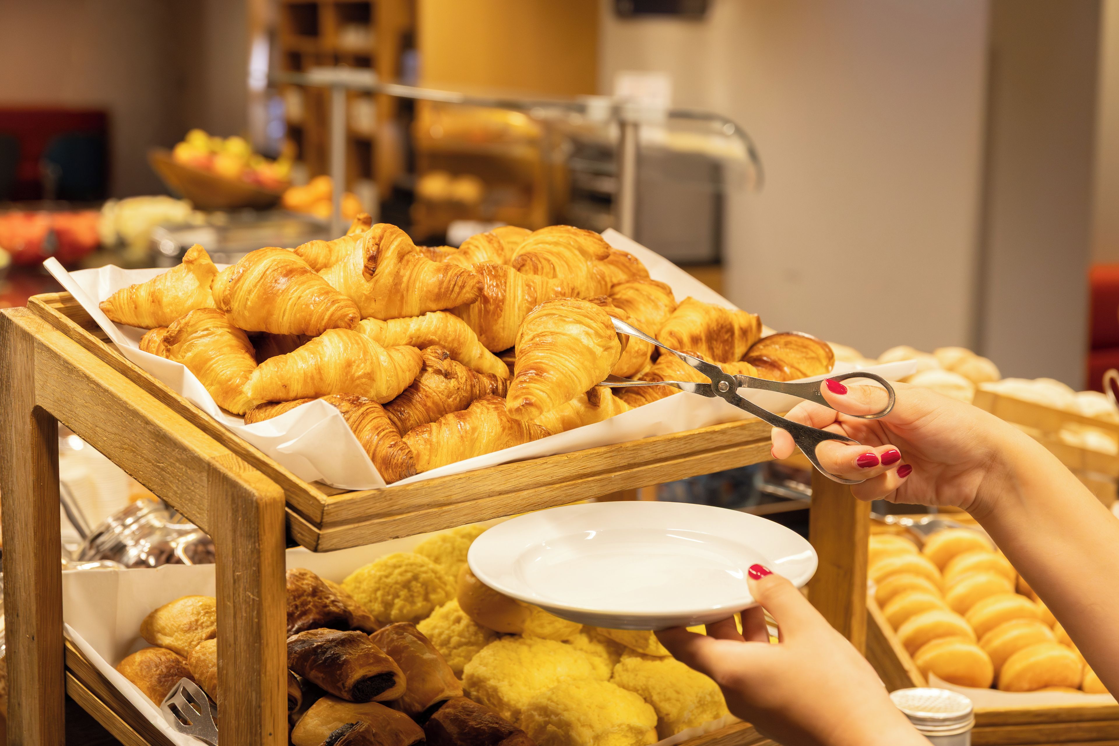 Een buffet met diverse gebakjes, waaronder croissants en muffins, en een persoon die een gebakje snijdt met een schaar.