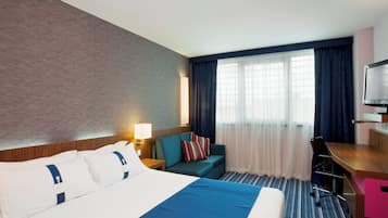A hotel room with a bed, a desk, a chair, a TV, and a window with curtains.