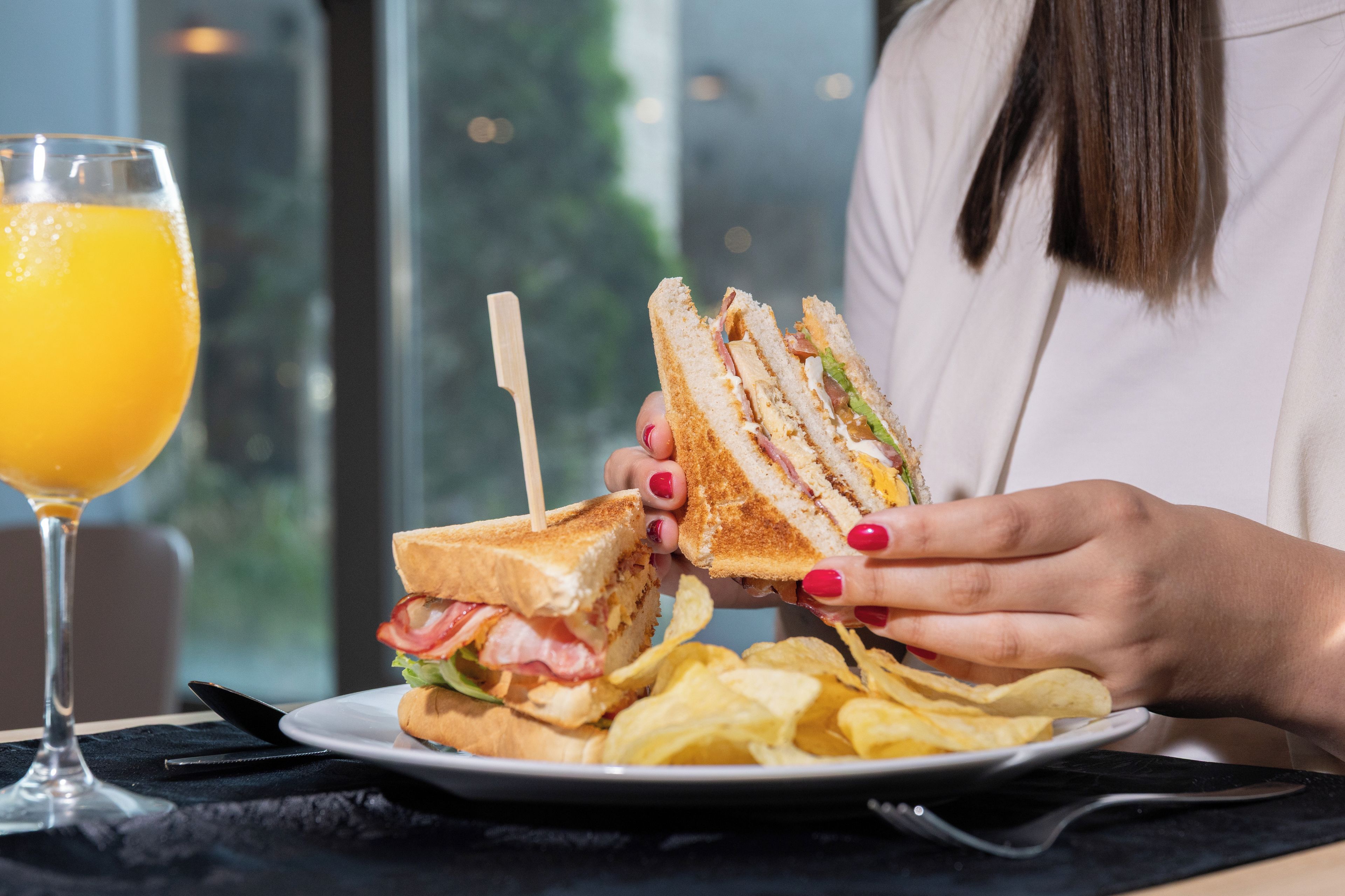 Una persona aguantant un entrepà amb un pal de draps, un got de suc de taronja i un plat de patates fregides damunt d'una taula.