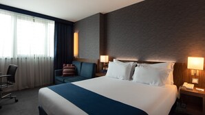 Una habitación de hotel con una cama grande, un escritorio, una silla y una ventana con cortinas.