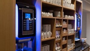 Una máquina de café con pantalla digital, rodeada de estantes llenos de tazas y vasos blancos.