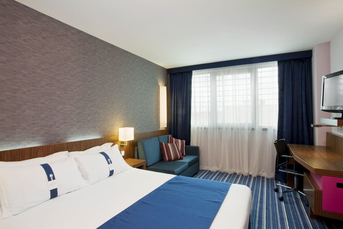 Ett hotellrum med en stor säng, ett skrivbord, en stol, en soffa och en tv.