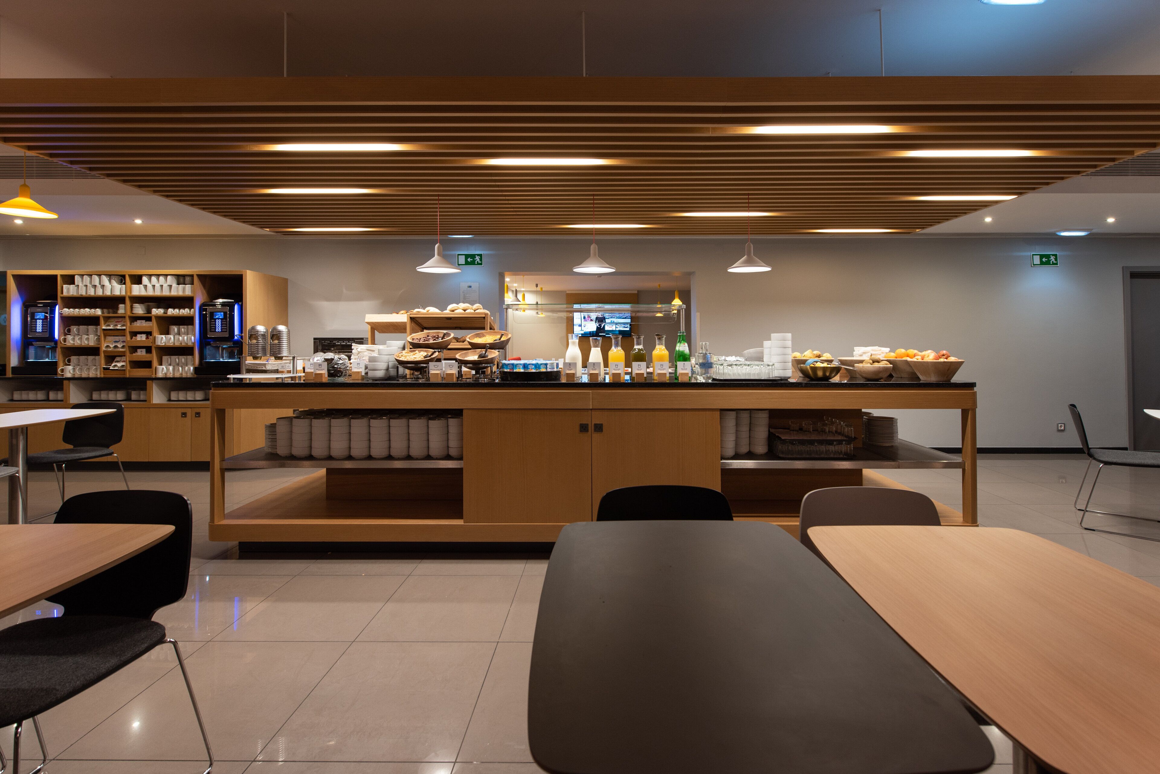 Una cafetería moderna con mostrador central, zona de estar y diversas opciones de comida y bebidas.