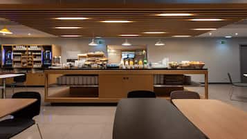 Una cafetería moderna con mostrador central, zona de estar y diversas opciones de comida y bebidas.