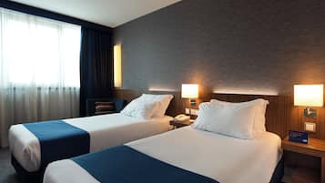 A hotel room with two beds, a nightstand with a lamp, a telephone, and a sign indicating the room number.