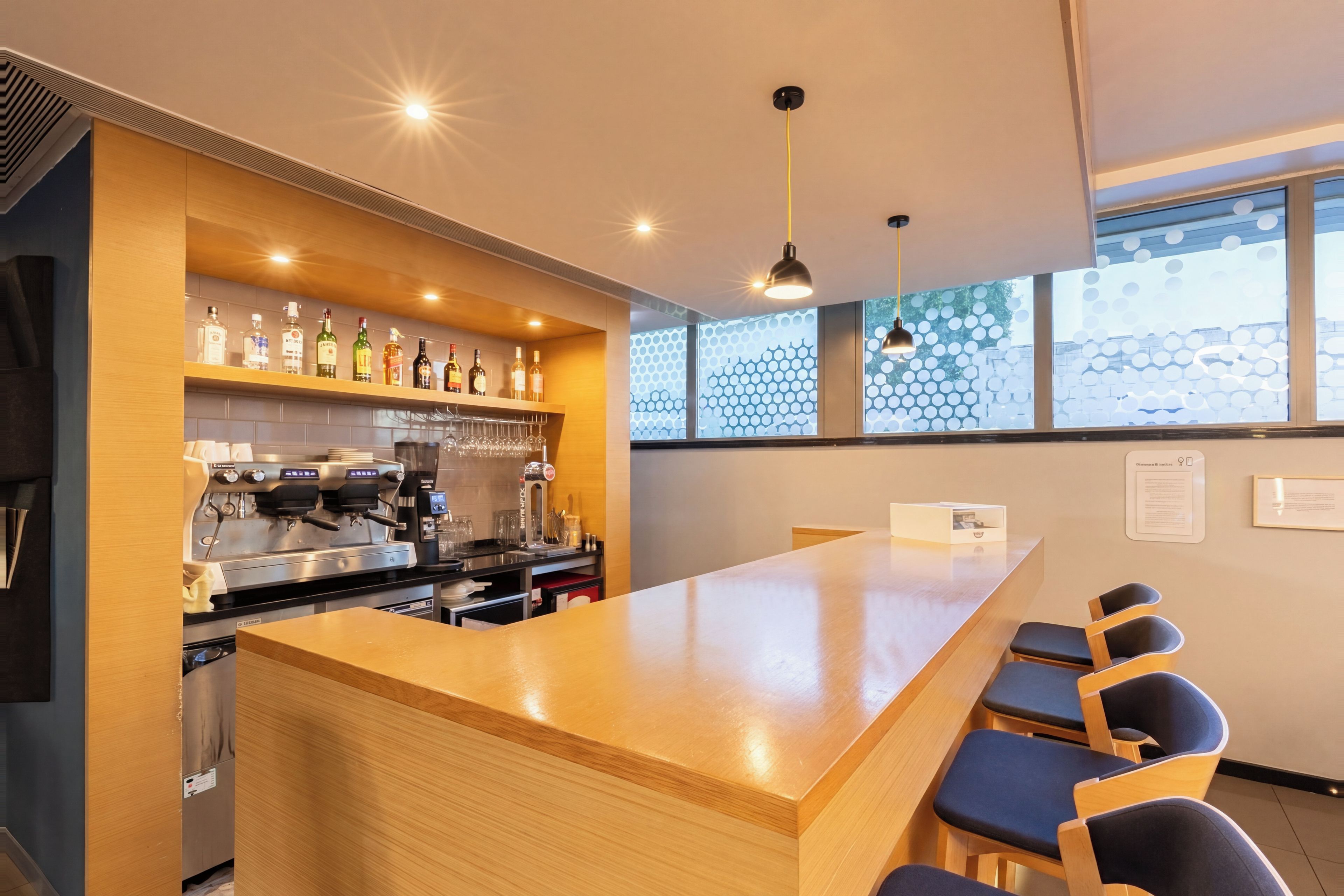 Un espace bar moderne doté d’un long comptoir, de tabourets de bar, d’une machine à café et d’un assortiment de bouteilles d’alcool.