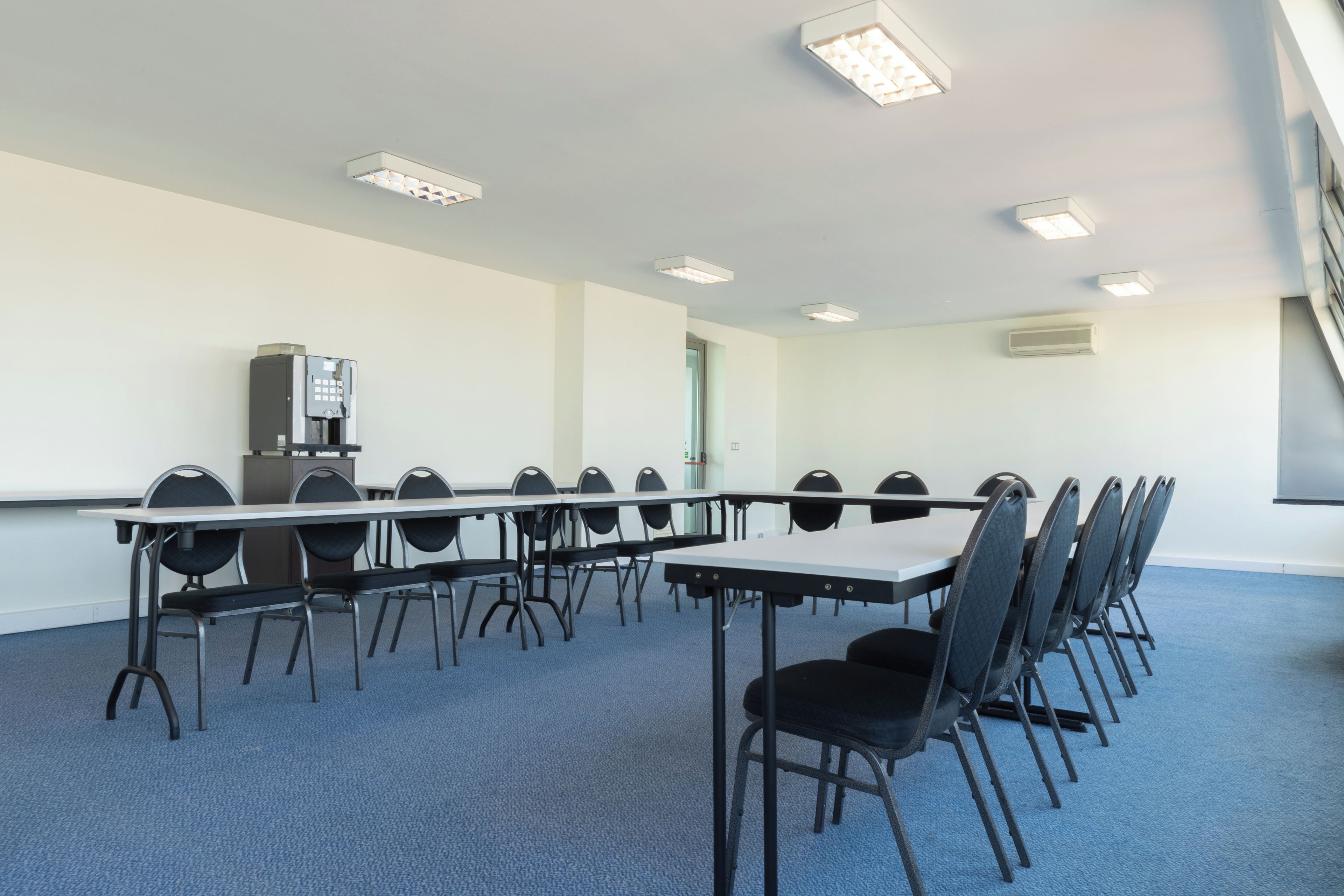 A conference room with a long table, chairs, a water dispenser, and ceiling lights.