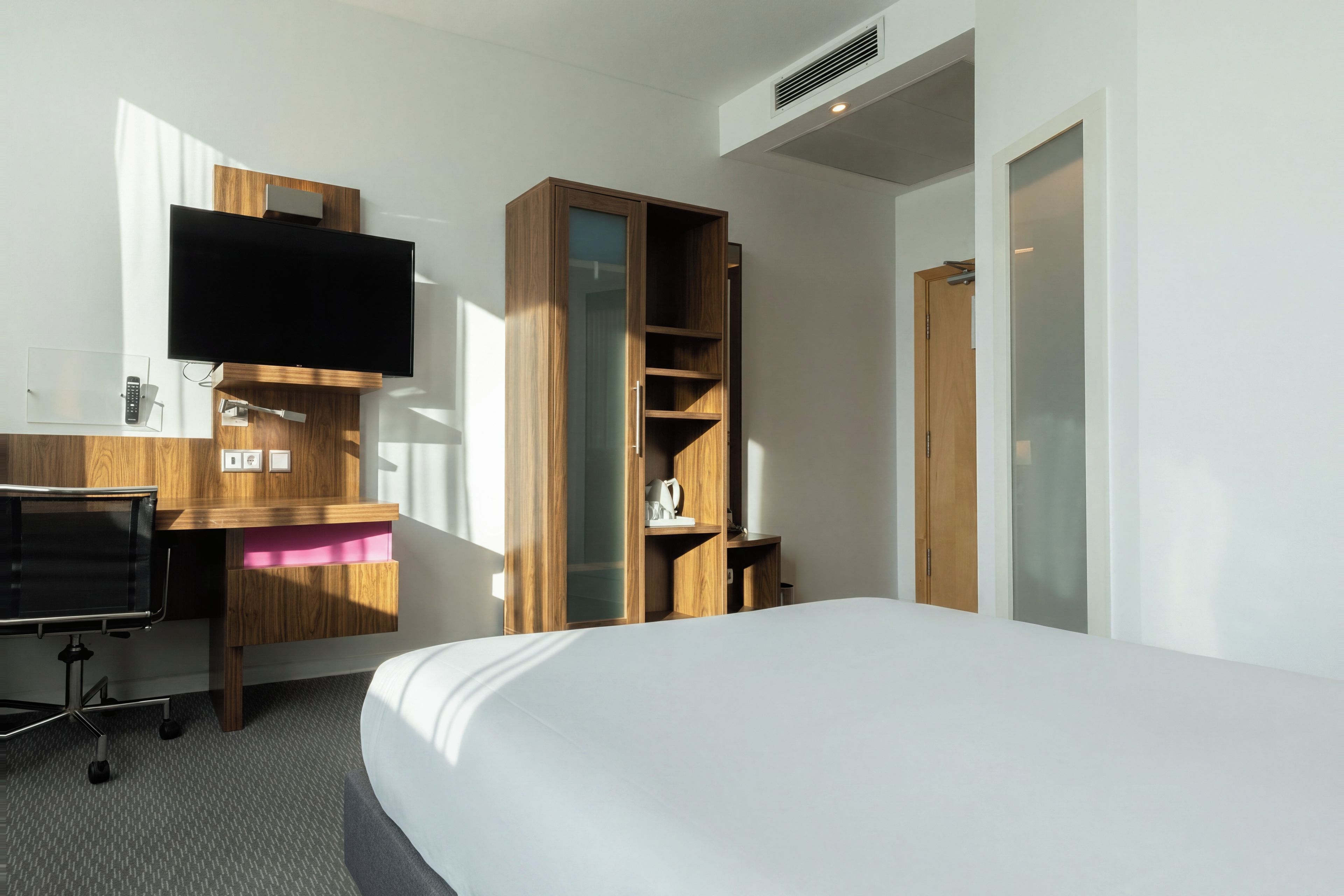 Habitación de hotel con cama, escritorio con televisor de pantalla plana, armario de madera y una puerta.