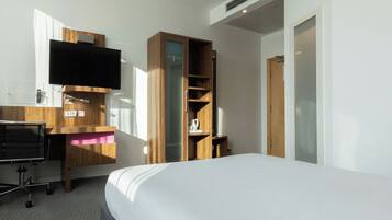 Habitación de hotel con cama, escritorio con televisor de pantalla plana, armario de madera y una puerta.