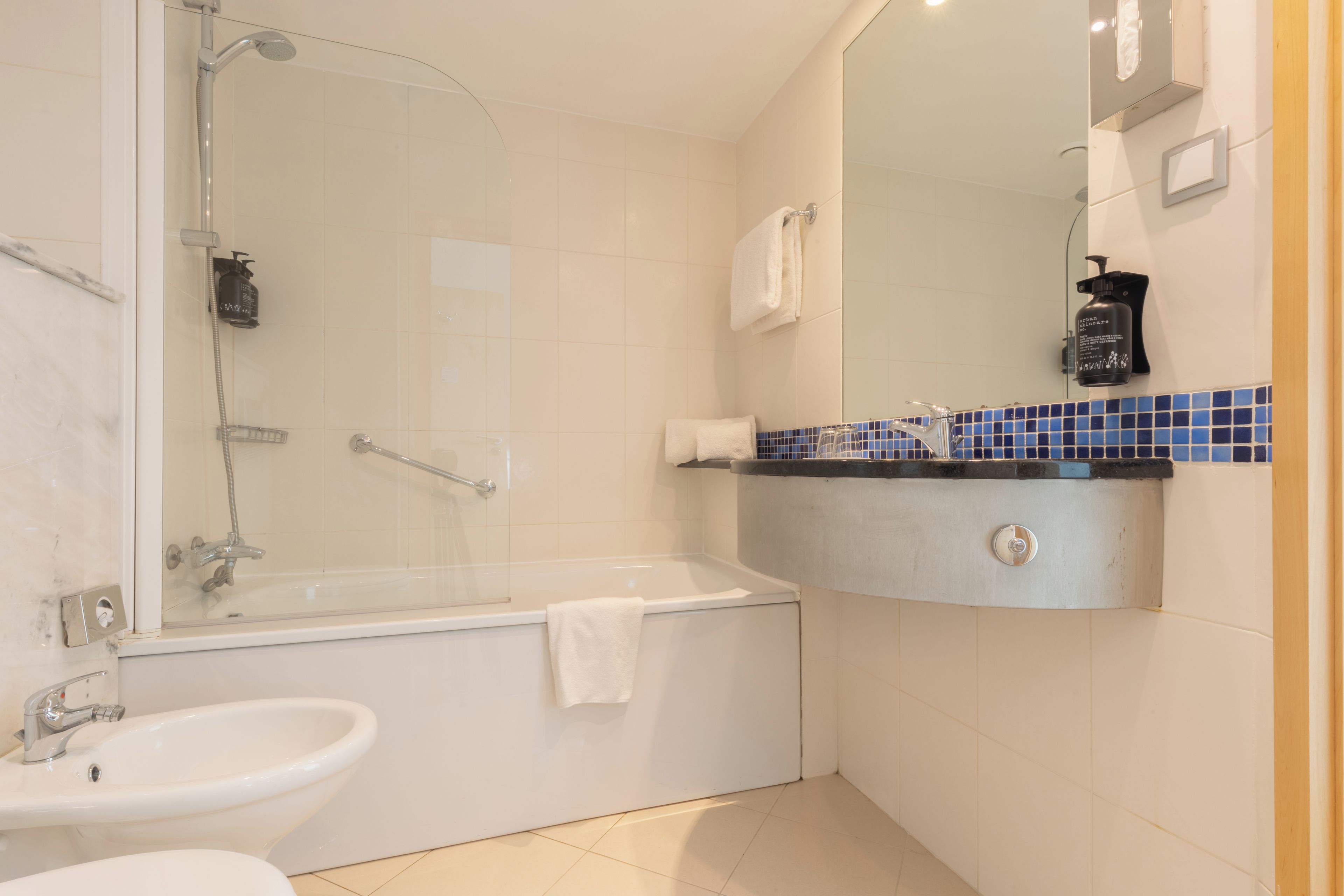 Un baño moderno con ducha de vidrio, bañera, lavamanos y tocador con espejo.