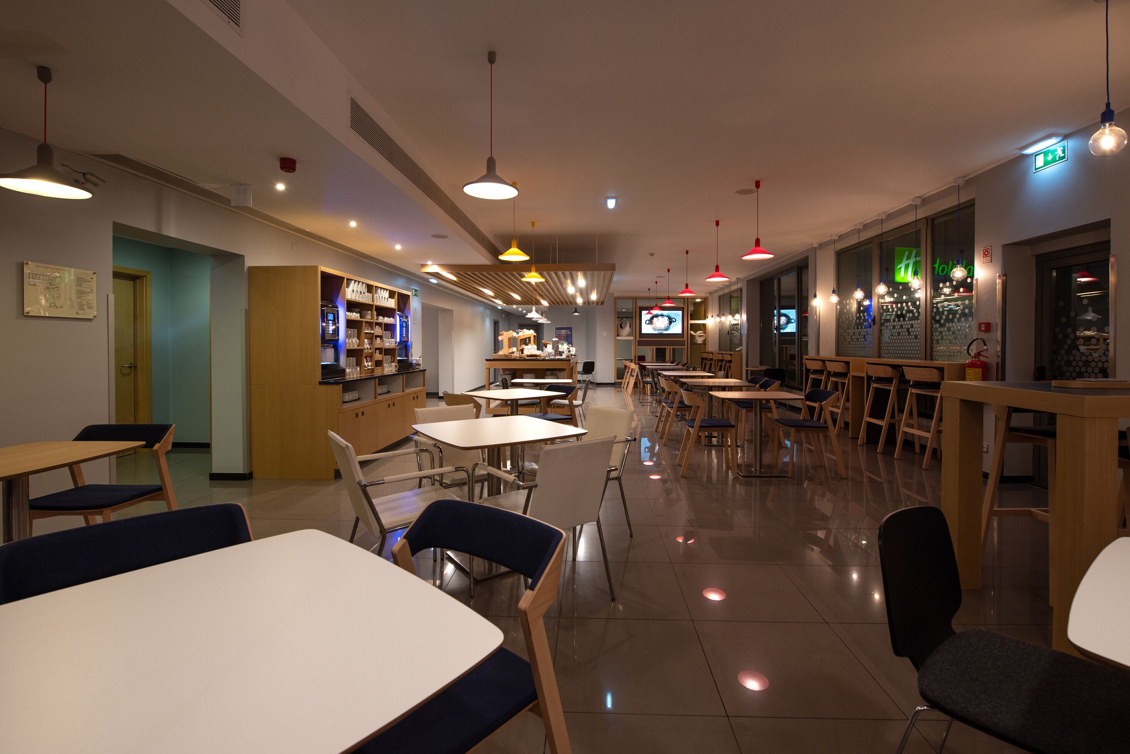 Un restaurante moderno con varias mesas y sillas, un área de cocina y una pantalla de televisión.