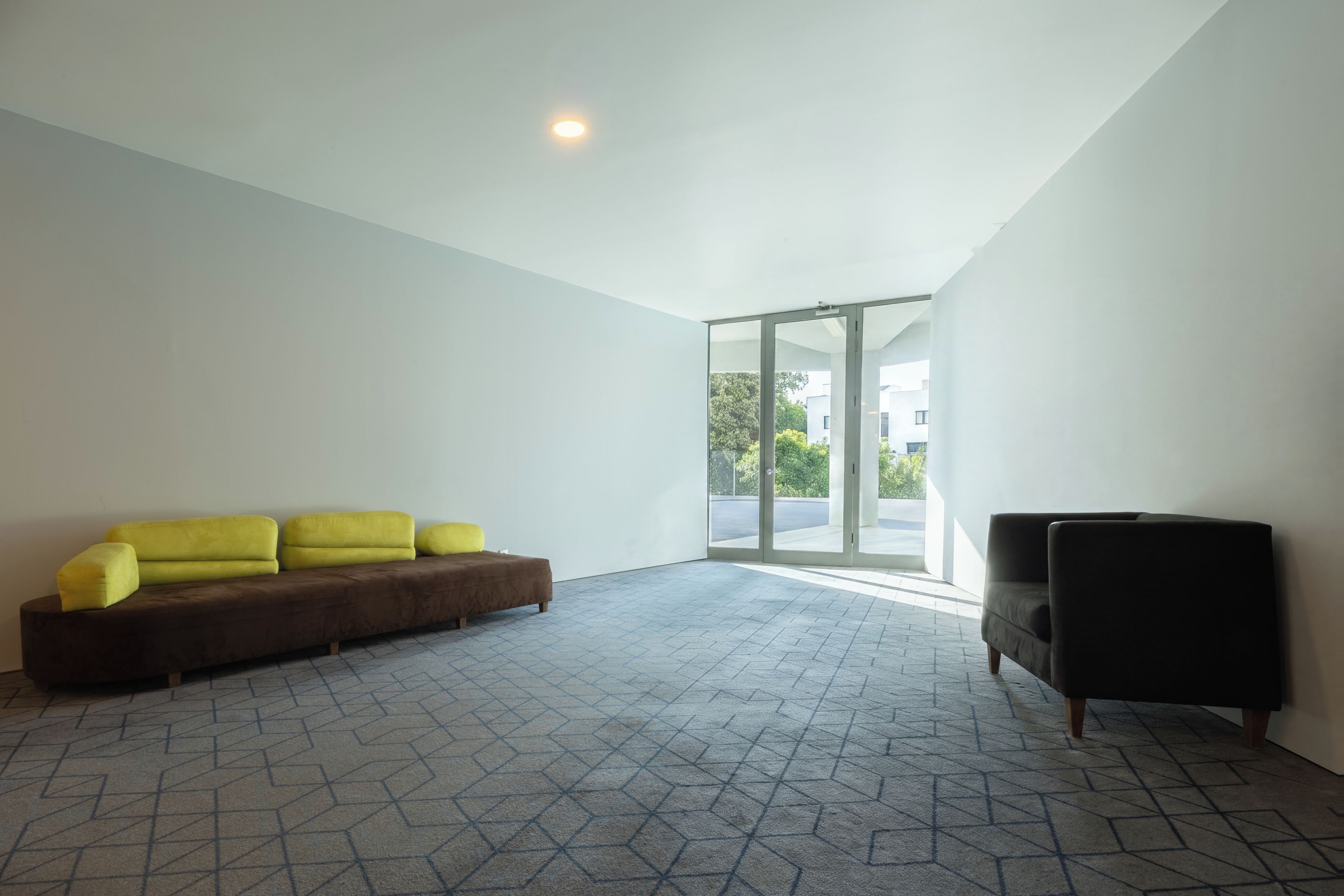 Une pièce moderne avec un sol à motifs géométriques, un canapé marron, un fauteuil jaune et un fauteuil noir.