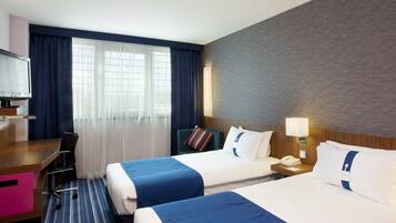 A hotel room with two beds, a desk, a chair, a TV, and a window with curtains.