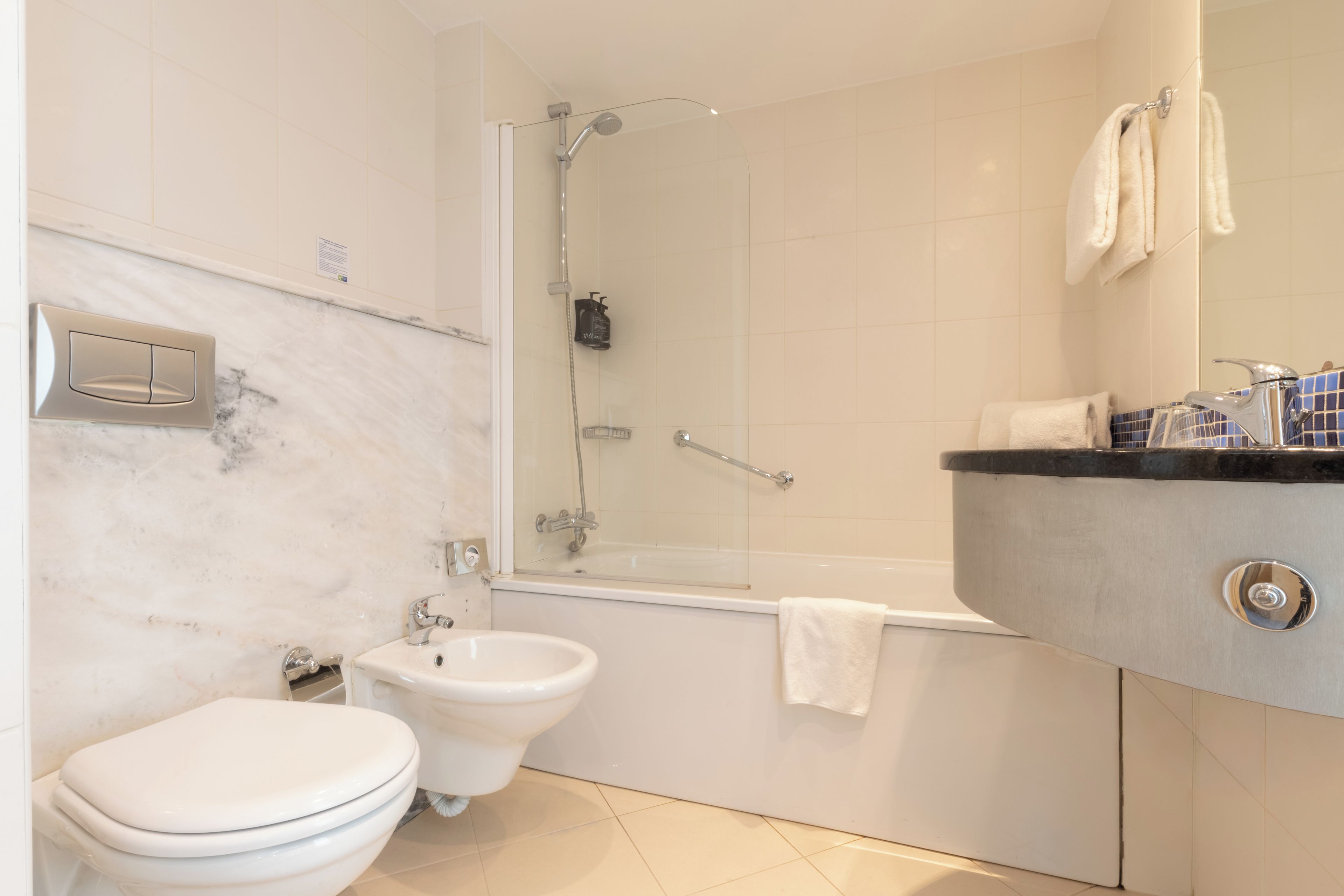 A bathroom with a toilet, bidet, bathtub, and a vanity with a mirror.