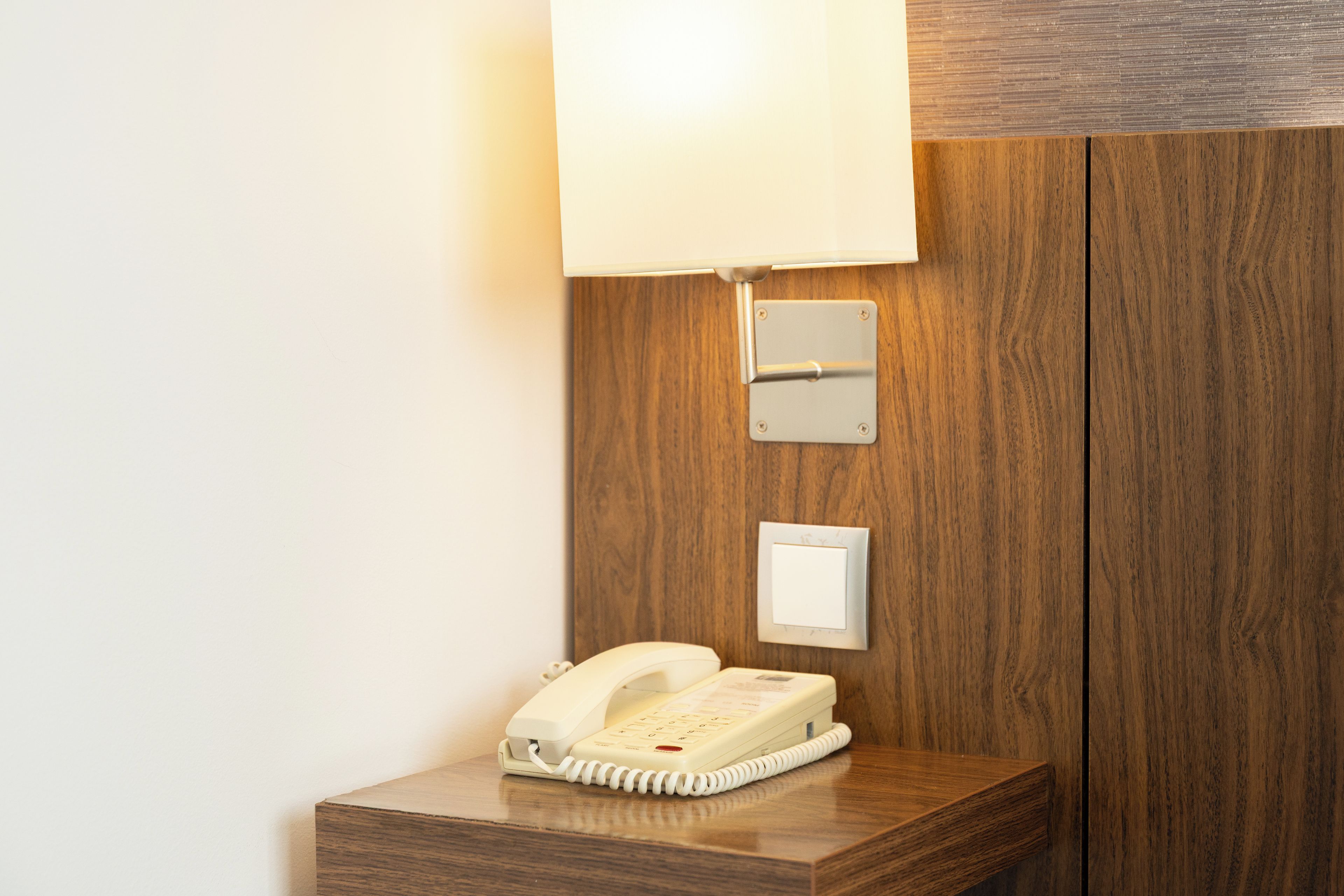 Un mostrador de recepción de hotel con un teléfono, una lámpara de pared y un enchufe.