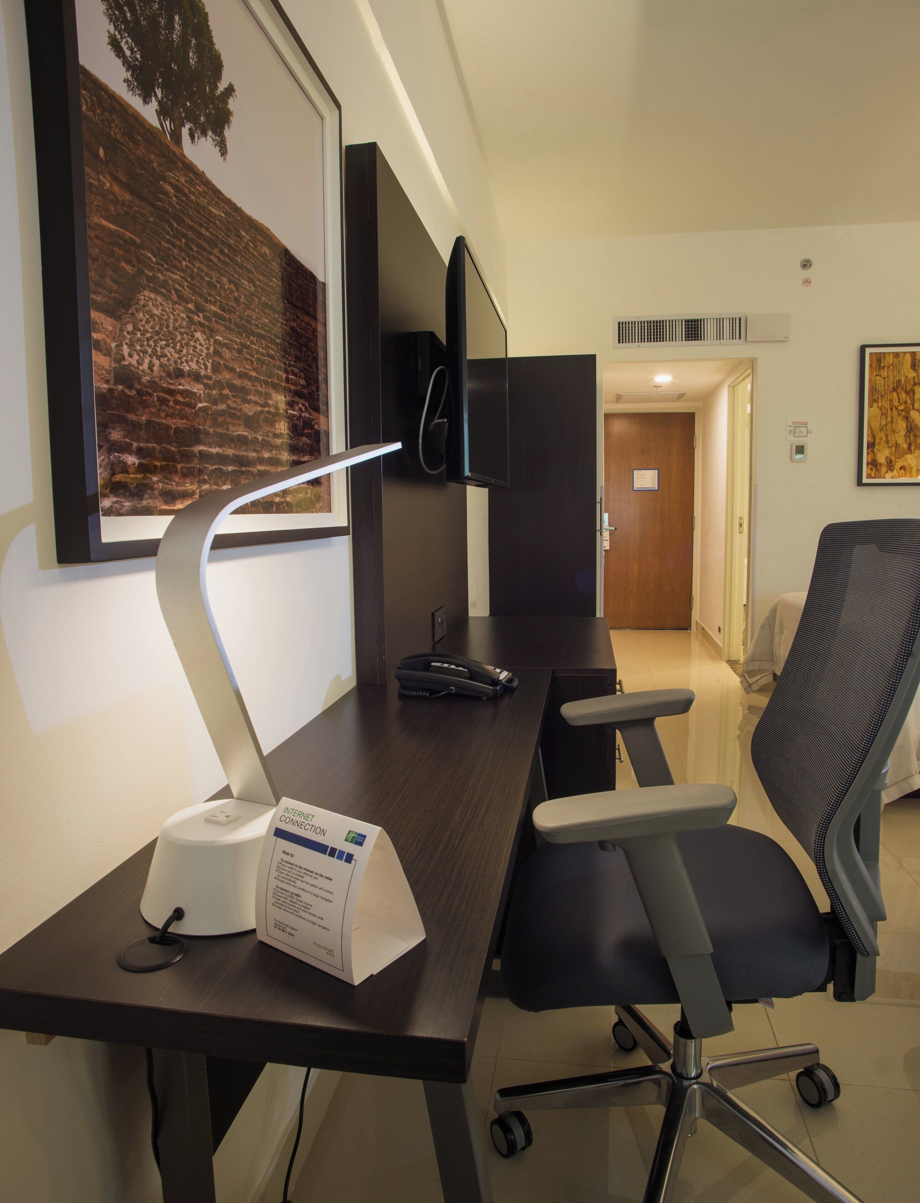 A modern office space with a desk, chair, computer monitor, and a framed picture on the wall.
